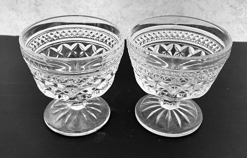 May include: Two clear glass dessert bowls with intricate diamond and starburst patterns. The bowls have a wide, decorative rim and sit on a stemmed base. The glass has a classic, elegant design, suitable for serving desserts.