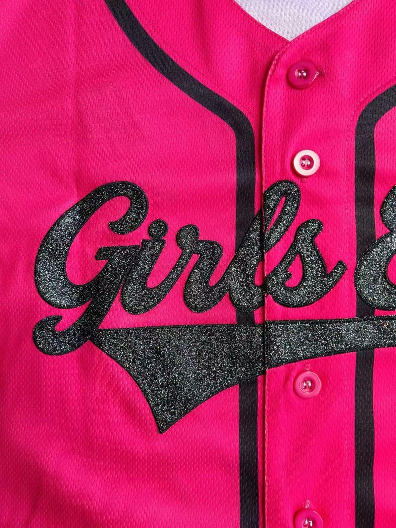May include: A bright pink baseball jersey with the word "Girls" in large, glittery black letters across the front. The jersey has black stripes along the button placket and collar, with matching black trim. Pink buttons secure the front.