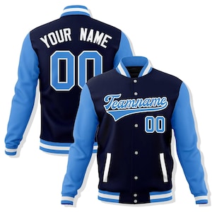 May include: Navy blue and light blue varsity jacket with white accents. The jacket features light blue sleeves, a navy body, and the text "Teamname" and "00" on the front. The back of the jacket displays "YOUR NAME" and "00".