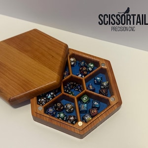 May include: Hexagonal wooden dice box with a cherry finish, open to reveal a blue interior and a collection of colourful polyhedral dice. The lid is open, and the box is labeled "SCISSORTAIL PRECISION CNC".