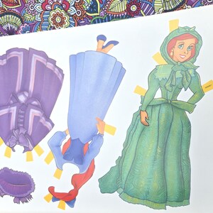 May include: A paper doll set with a green dress, a purple jacket, and a blue dress with a red scarf. The paper doll has a green dress and bonnet. The set is on a white background.
