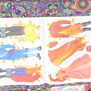May include: An open book displaying paper dolls of historical figures. The dolls are dressed in outfits of yellow, blue, red, and orange. The paper dolls are cut out and ready to be played with.
