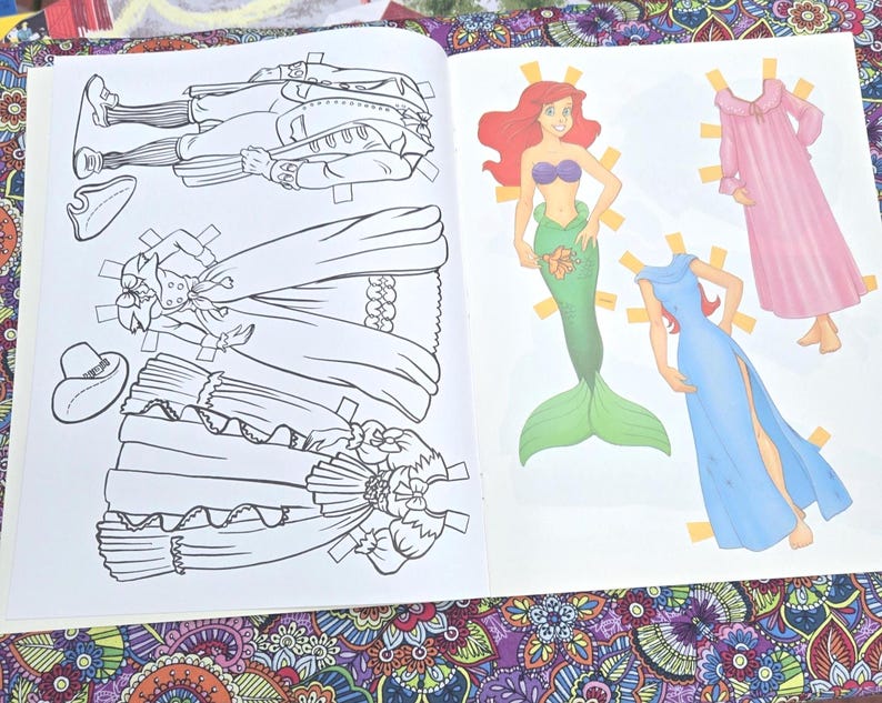 May include: An open paper doll book with illustrations of paper dolls and their outfits. The left page shows black and white line drawings of a man and two dresses. The right page shows a mermaid and two dresses in colour.
