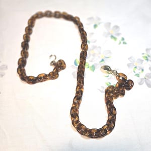 May include: A vintage necklace featuring large, oval-shaped links in a translucent, tortoiseshell-like pattern. The chain is a warm brown color and has a silver-tone clasp.