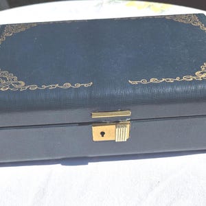 May include: A rectangular, dark blue jewelry box with gold-colored filigree corner accents and a gold-toned clasp. The box has a textured surface and a rectangular shape, suggesting it is designed for storing jewelry.