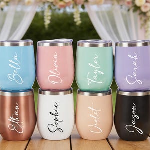 May include: Eight stemless wine tumblers in various colors, including blue, pink, mint green, and purple, each with a silver rim and a name in a cursive font. The bottom row features copper, white, peach, and black tumblers, also with names.