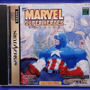 May include: Marvel Super Heroes Sega Saturn game case. The cover features Captain America in a blue and red suit, with other Marvel characters in the background. The game title is in large red letters. The Sega Saturn logo is on the side.