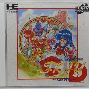 May include: A video game cartridge for the Super CD-ROM System, featuring a colorful illustration of a female character with blue hair and a red dress, surrounded by various fantasy creatures. The title of the game is "Xak", with the subtitle "In Magical Adventure".