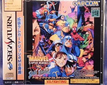 Puede incluir: Caja de juego de Sega Saturn para "Marvel Super Heroes vs. Street Fighter". La carátula presenta un collage de personajes de cómics, incluyendo al Capitán América, Spider-Man y Chun-Li. La caja está en una funda de plástico transparente.