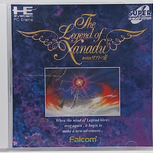 May include: A CD case for the Super CD-ROM System video game "The Legend of Xanadu: Island of Legend". The case features a colorful image of a fiery sky with a glowing orb in the center. The text "The Legend of Xanadu" is written in a stylized font.