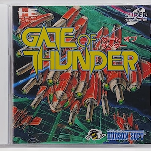 May include: A video game cartridge for the Super CD-ROM System. The game is called "Gate of Thunder" and features a red and silver spaceship with a green background. The game is published by Hudson Soft.