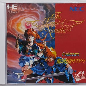 May include: A video game cartridge for the PC Engine console. The game is The Legend of Xanadu, a role-playing game by Falcom. The cartridge is red and blue with a picture of two characters, a woman with long red hair and a man with short brown hair. The text on the cartridge reads "The Legend of Xanadu", "Falcom", "風の伝説ザナドゥ", and "SUPER CD-ROM SYSTEM".