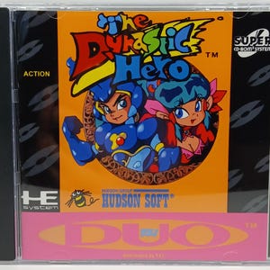 May include: A CD-ROM case featuring the game "The Dynastic Hero." The cover art showcases two cartoon characters in blue and pink, set against an orange background. The case includes the "SUPER CD-ROM SYSTEM" logo and the "HUDSON SOFT" logo.
