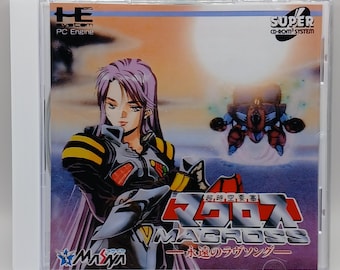 Puede incluir: Una caja de juego de video para el Super CD-ROM System para la PC Engine. La caja presenta una ilustración colorida de un personaje femenino en un entorno futurista con un gran logotipo rojo y blanco que dice "Macross" en japonés e inglés. El texto "超時空要塞" también es visible en la caja, que se traduce como "Fortaleza Dimensional Superior".