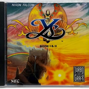 May include: A Ys Book I & II video game case. The cover art features a woman with large wings, a castle, and a rainbow against a yellow and orange sky. The text "NIHON FALCOM" and "TURBO GRAFX" are visible.