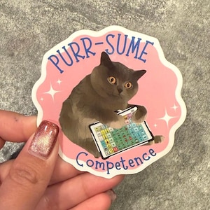May include: A sticker featuring a gray cat holding a tablet with colorful buttons. The sticker has a pink background with the words "PURR-SUME" and "Competence" in blue and white. The cat has yellow eyes.
