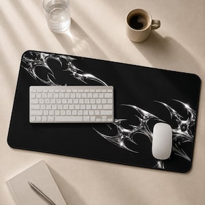 May include: A rectangular black desk mat featuring a metallic silver liquid-like abstract pattern in the corners. The mat is positioned under a white wireless keyboard and a white computer mouse, providing a smooth surface for office equipment.