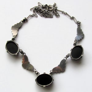 May include: Silver-toned necklace featuring three oval black stones and decorative butterfly-shaped accents. The necklace has a delicate chain and a secure clasp. The design is symmetrical, with the stones evenly spaced along the chain.