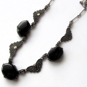 May include: A vintage-style necklace featuring oval black gemstones and ornate silver-tone metalwork. The necklace has a delicate chain and decorative filigree elements, creating an elegant and classic look. The gemstones are set in a bezel setting.