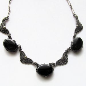 May include: A vintage-style necklace featuring oval black gemstones set in an ornate, dark metal filigree design. The necklace has a symmetrical arrangement with three prominent central stones and decorative accents.