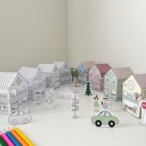 May include: A collection of paper town buildings, cars, trees, and people. The buildings include a bakery and flower shop. The town is decorated with signs and a stop sign. Colored pencils are in the foreground.