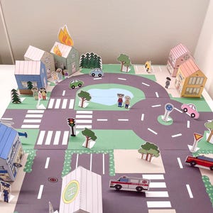 May include: A colorful paper city playset with roads, buildings, trees, cars, and people. The set includes a fire, a police station, an ambulance, and a helipad. The buildings are various colors, and the cars are green, pink, and red.
