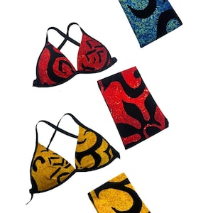 May include: Three bikini tops and three matching rectangular fabric pieces in blue, red, and yellow. Each piece features a black abstract pattern over a textured, speckled background. The bikini tops have thin black straps and a triangular shape.