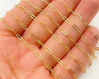 May include: Close-up of a delicate gold-colored chain with an elongated oval link design. The chain is held in a hand, showcasing its fine details and reflective surface. The jewelry piece is likely for necklaces or bracelets.