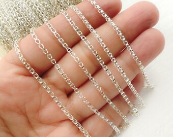 Puede incluir: Primer plano de un rollo de cadena de color plateado. Varios hilos de la cadena se sostienen en una mano, mostrando los delicados eslabones interconectados. La cadena se utiliza probablemente para la fabricación de joyas u otros proyectos de artesanía.