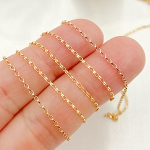 May include: Delicate gold-colored chain necklace with an oval link design. The chain is displayed against a light background, highlighting its shiny, reflective surface. The necklace is a fine piece of jewelry.