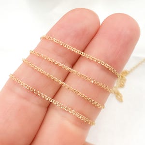 May include: Close-up of a delicate gold chain necklace. The chain is made of small, interconnected links, creating a fine, textured appearance. The warm gold color contrasts against the background. The chain is likely for jewelry making or personal wear.