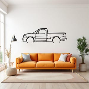 May include: Black metal wall art depicting a side profile of a pickup truck. The artwork is mounted on a white wall above an orange sofa. The truck's design is minimalist, with clean lines and a focus on the vehicle's silhouette.