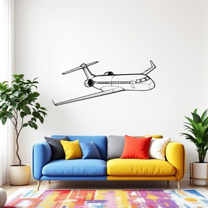 May include: A black and white line drawing of a passenger airplane is mounted on a white wall. The plane has wings, a tail, and a detailed fuselage. Below the plane is a colorful sofa with blue, yellow, and gray sections, and a patterned rug.