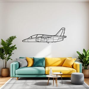 May include: Black outline of a jet airplane mounted on a white wall. The artwork is above a teal and yellow sofa with colorful pillows. Potted plants and a small table with a white vase are in front of the sofa.