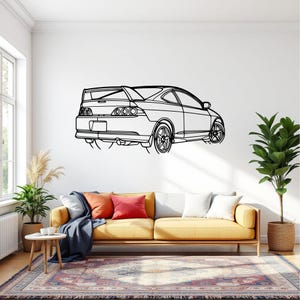 Puede incluir: Dibujo lineal en blanco y negro de un coche deportivo montado en una pared blanca. El coche tiene un alerón, llantas de aleación y una parte trasera detallada. La obra de arte se exhibe sobre un sofá amarillo con cojines coloridos y una alfombra estampada.