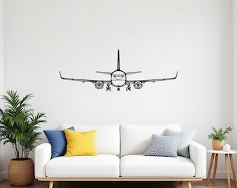 May include: Black metal airplane wall art. The airplane is depicted in a minimalist style, with a focus on the outline of the aircraft. The wings are extended, and the landing gear is visible. The artwork is mounted on a white wall above a white sofa.