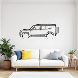 May include: Black line drawing of a sport utility vehicle (SUV) mounted on a white wall. The SUV has a spare tire on the back. The wall art is above a white couch with colorful pillows and a potted plant.