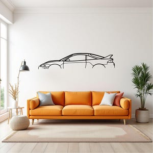 Puede incluir: Contorno negro de un coche deportivo montado en una pared blanca sobre un sofá naranja. El coche presenta un alerón y un diseño elegante. La habitación incluye una lámpara de pie, una mesa auxiliar, una alfombra y una planta en maceta.