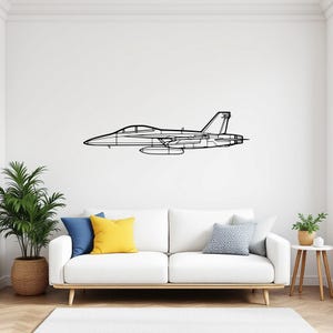 Pode incluir: Arte de parede em metal preto que retrata um contorno detalhado de um caça. A obra de arte é montada em uma parede branca acima de um sofá branco com almofadas coloridas e uma planta em vaso, criando um moderno destaque de decoração.