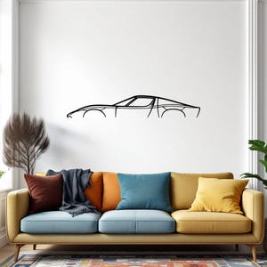 May include: A black metal wall art piece depicting the side profile of a classic sports car. The artwork is a minimalist line drawing, mounted on a white wall above a yellow sofa with colorful pillows. The car's design is sleek and aerodynamic.