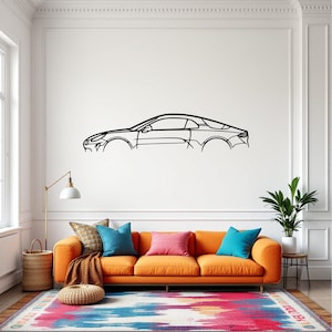Puede incluir: Un diseño de línea negra de un coche en una pared blanca sobre un sofá naranja con almohadas de colores. El sofá está frente a una pared blanca con una lámpara de pie dorada y una planta verde en maceta.