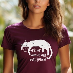 May include: A maroon t-shirt featuring a white graphic of a sleeping cat with a heart and the text "ask me about my best friend". The shirt has short sleeves and a crew neck.