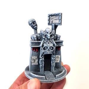 Puede incluir: Un edificio en miniatura impreso en 3D con un diseño de calavera. El edificio es gris y tiene un letrero que dice "Captain Skulldings Fun Park".