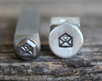 May include: Two metal stamps with a design of an envelope with a heart inside. The stamps are used for stamping metal or leather.
