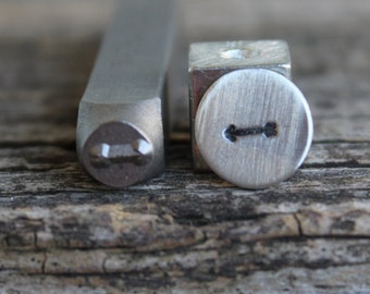 May include: Two metal stamps for jewelry making. The stamp on the left is a rectangle with a rounded edge and a small arrow design. The stamp on the right is a round stamp with a larger arrow design.