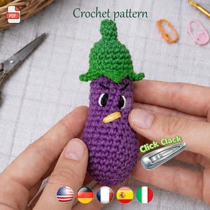 May include: A handmade crochet eggplant with a green leafy top and an angry face. The purple vegetable has white eyes, a yellow beak, and a stern expression. The image includes the text "Crochet pattern".