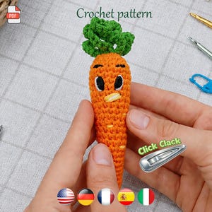 Puede incluir: Una zanahoria de ganchillo naranja hecha a mano con una parte superior verde y una cara de dibujos animados. El texto "Crochet pattern" está en la parte superior de la imagen. Una pinza para el pelo plateada con el texto "Click Clack" está en la imagen.