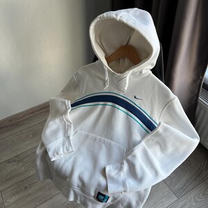 Puede incluir: Sudadera con capucha blanca con una franja azul y turquesa en el pecho. Cuenta con un bolsillo delantero y un peque&ntilde;o logotipo de Nike. La sudadera est&aacute; hecha de un material suave y tiene pu&ntilde;os y dobladillo acanalados.