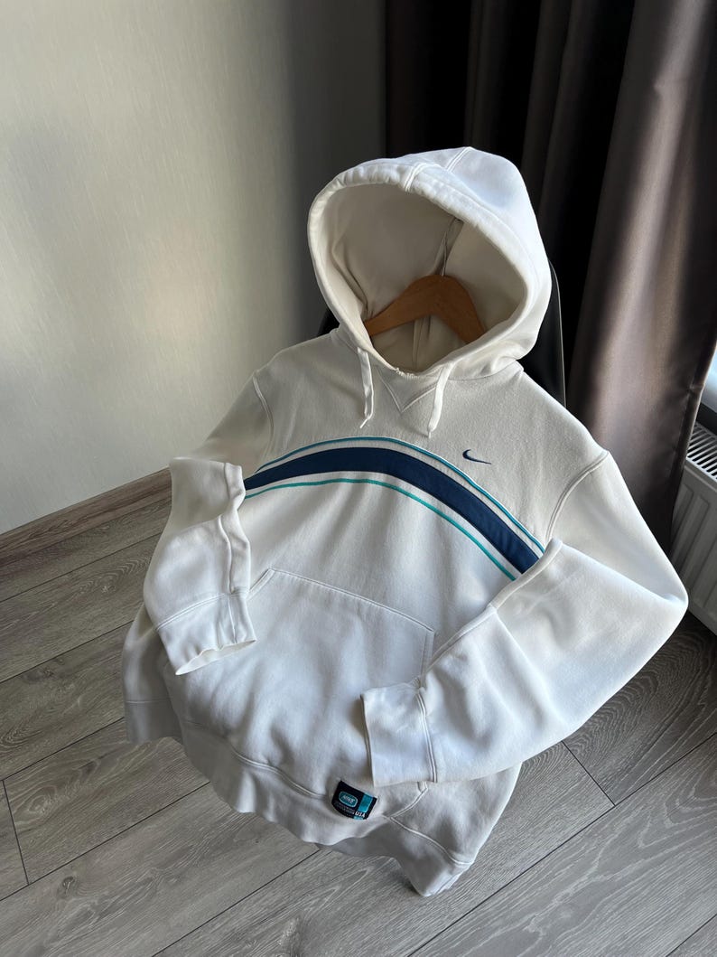 Puede incluir: Sudadera con capucha blanca con una franja azul y turquesa en el pecho. Cuenta con un bolsillo delantero y un peque&ntilde;o logotipo de Nike. La sudadera est&aacute; hecha de un material suave y tiene pu&ntilde;os y dobladillo acanalados.