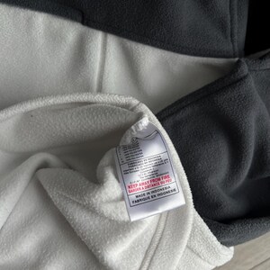 May include: A grey and white fleece pullover with a small red Nike logo. The garment has a tag that reads "KEEP AWAY FROM FIRE" and "MADE IN INDONESIA".